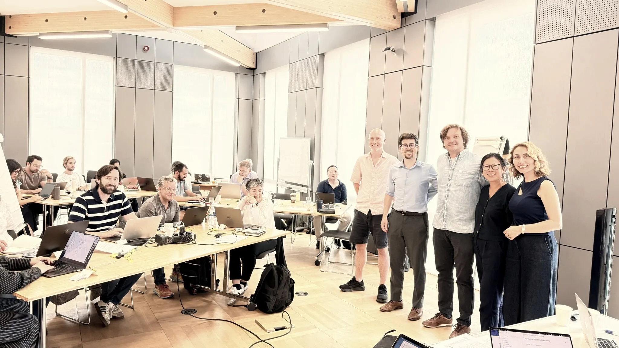A wide view of the seminar room during the first Oxford Agentic Bootcamp: attendees working at laptops along the tables, with five people standing together at the end of the day.