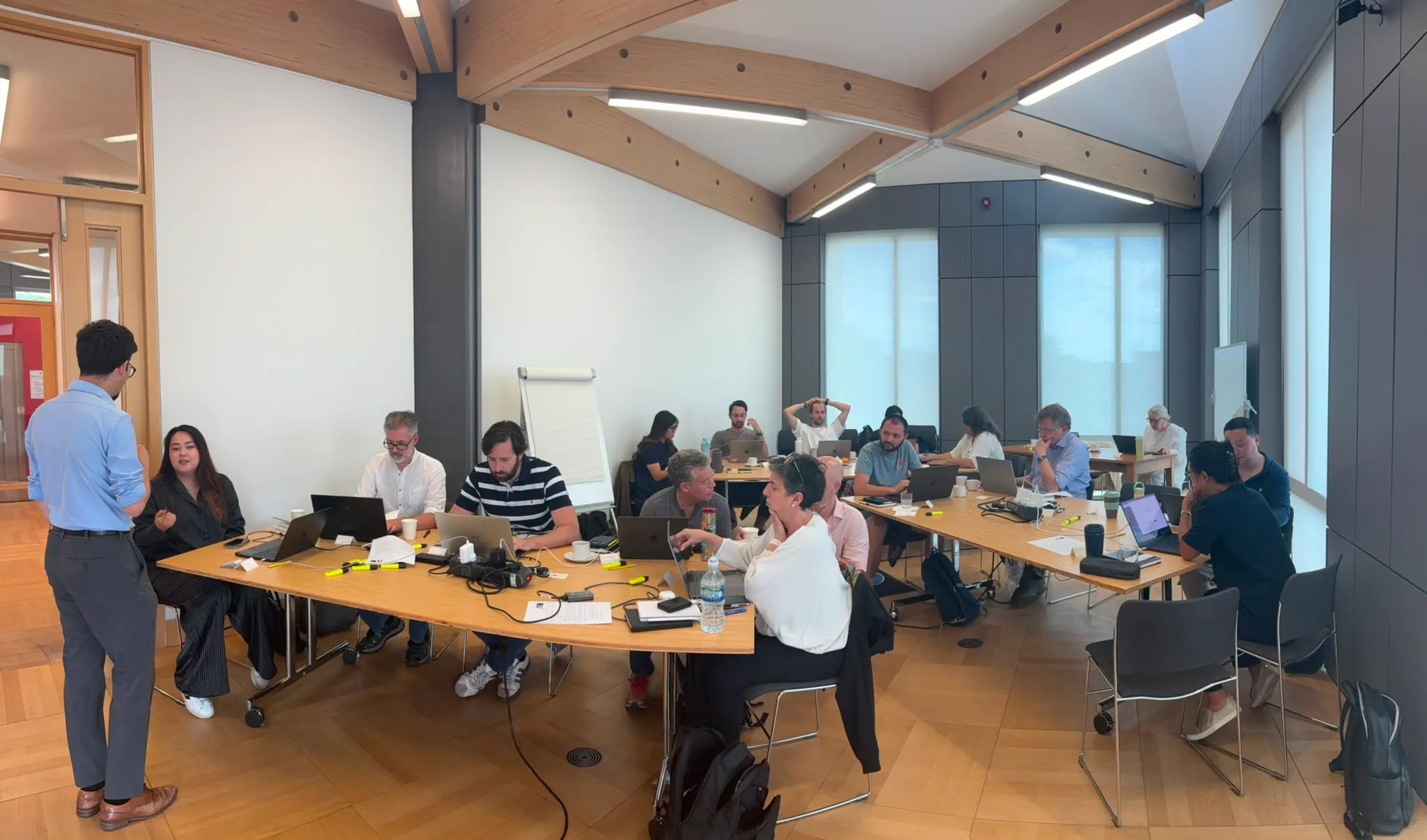Attendees working at long cabaret-style tables with laptops in a bright, vaulted seminar room at St Anne's College, Oxford, during the first Oxford Agentic Bootcamp.