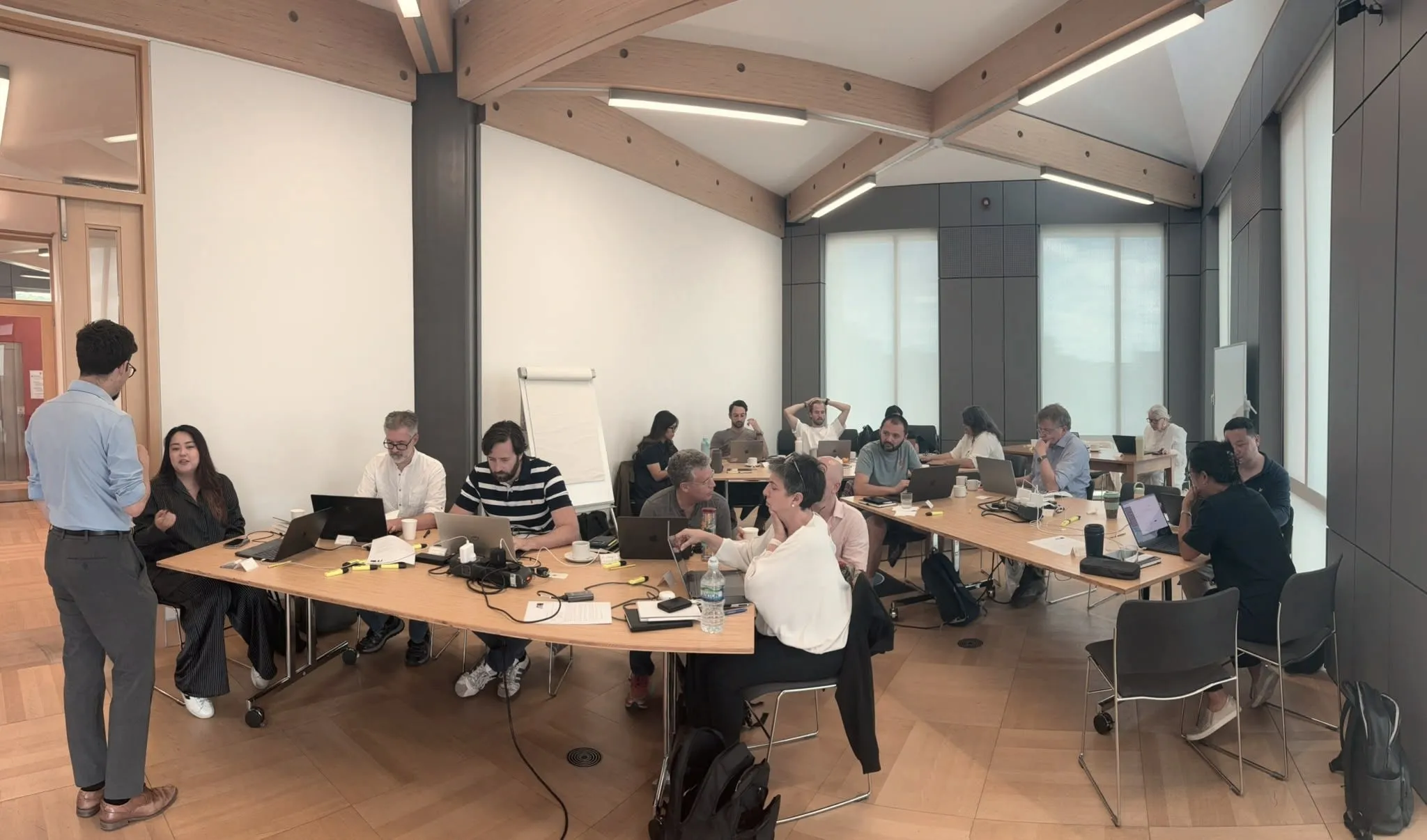 Attendees working at long cabaret-style tables with laptops in a bright, vaulted seminar room at St Anne's College, Oxford, during the first Oxford Agentic Bootcamp.